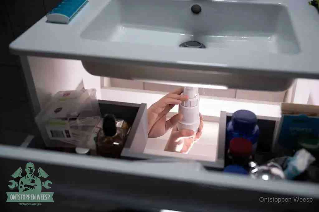 Een pompfles met zeep boven een wastafel, de heet water en afwasmiddel-methode om een vetprop in de afvoer los te maken in Weesp