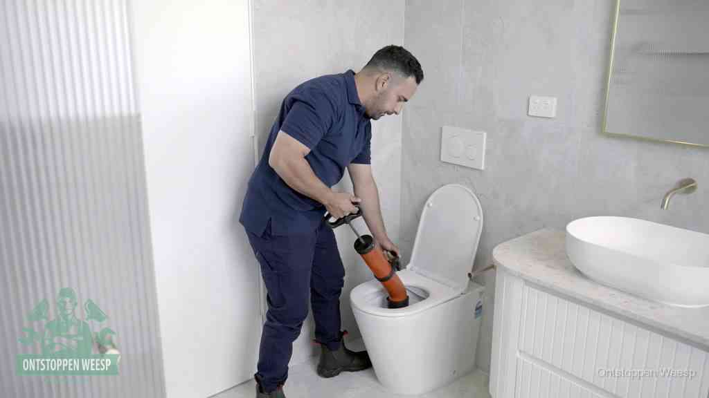 Een monteur buigt over een wandcloset en duwt met de hand een persluchtontstopper in de toiletpot om de verstopping handmatig los te maken in Weesp