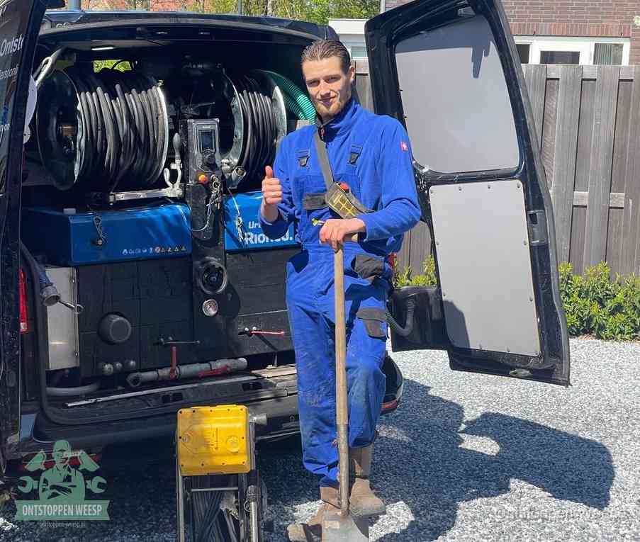 Een monteur bij de werkbus met grote hogedruk-slanghaspels, apparatuur voor hardnekkige afvoerverstoppingen in Weesp