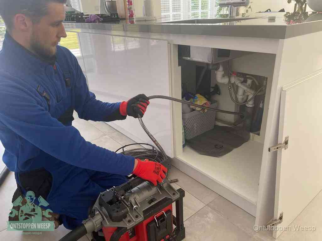 Monteur voert een ontstoppingsveer in de afvoer onder de keuken in Weesp