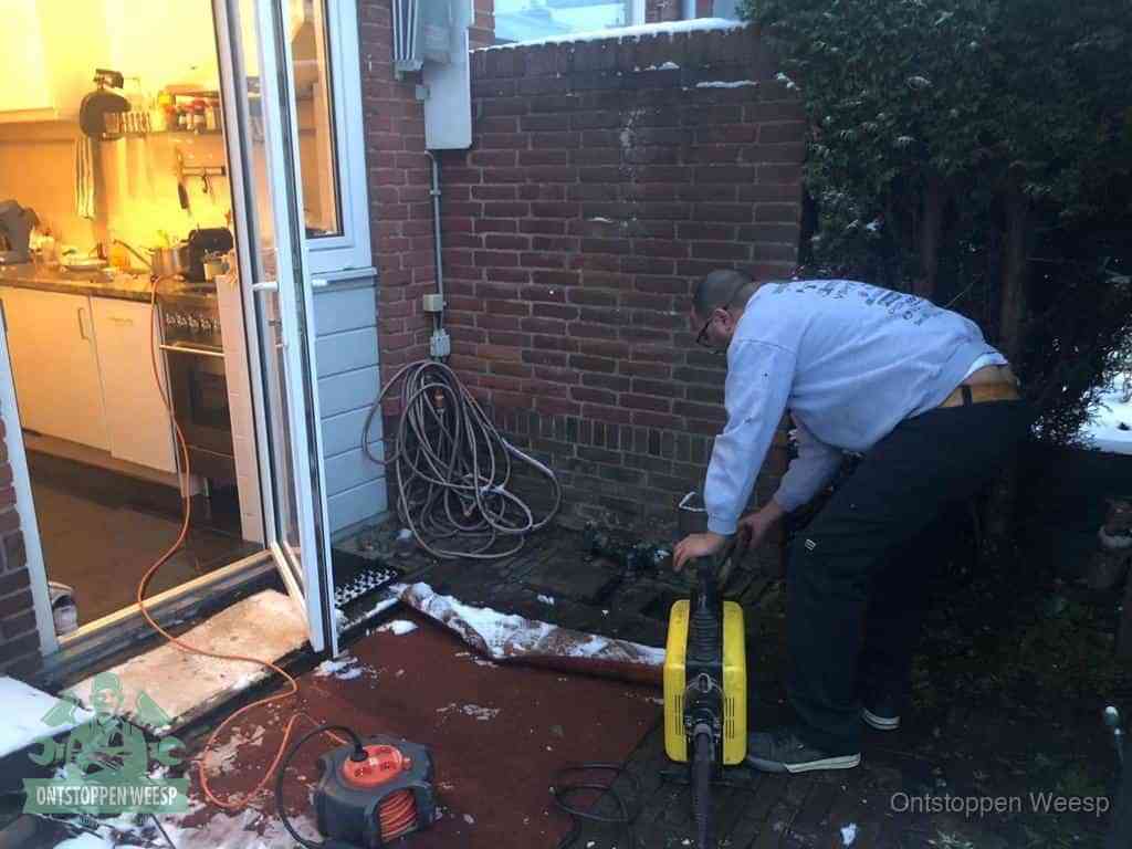 Een monteur werkt buiten bij een open riool-/grondput met een elektrische ontstoppingsmachine om een verborgen afvoerprobleem op te sporen in Weesp