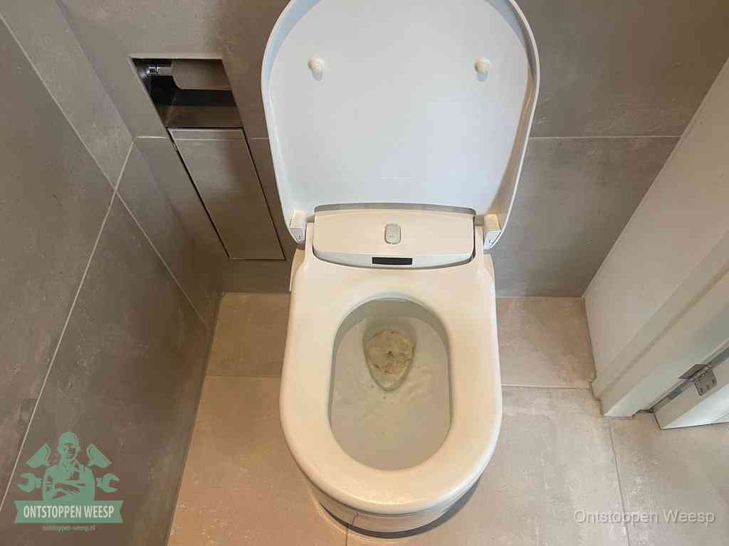 Een wit hangtoilet waarin een prop wc-papier op het water blijft drijven, een duidelijk signaal van een verstopte wc in Weesp