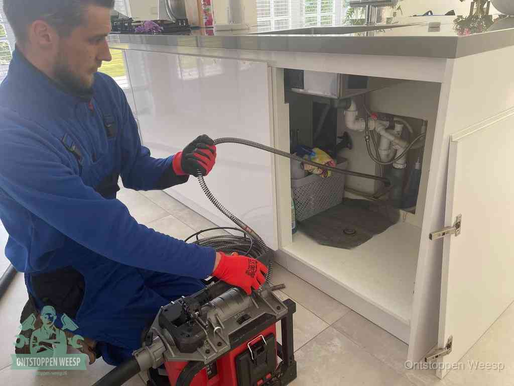 Een monteur reinigt de keukenafvoer grondig met een veermachine om terugkerende gootsteenverstoppingen te voorkomen in Weesp