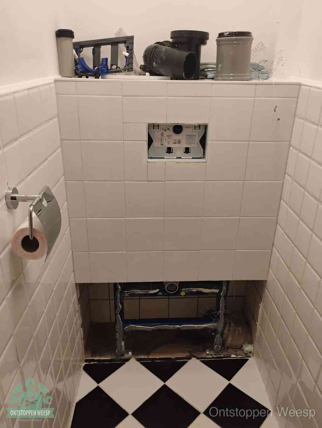 Een toiletruimte waar het hangtoilet en de inbouwreservoir-onderdelen zijn vrijgelegd voor onderhoud, periodiek nazicht voorkomt een wc-verstopping in Weesp